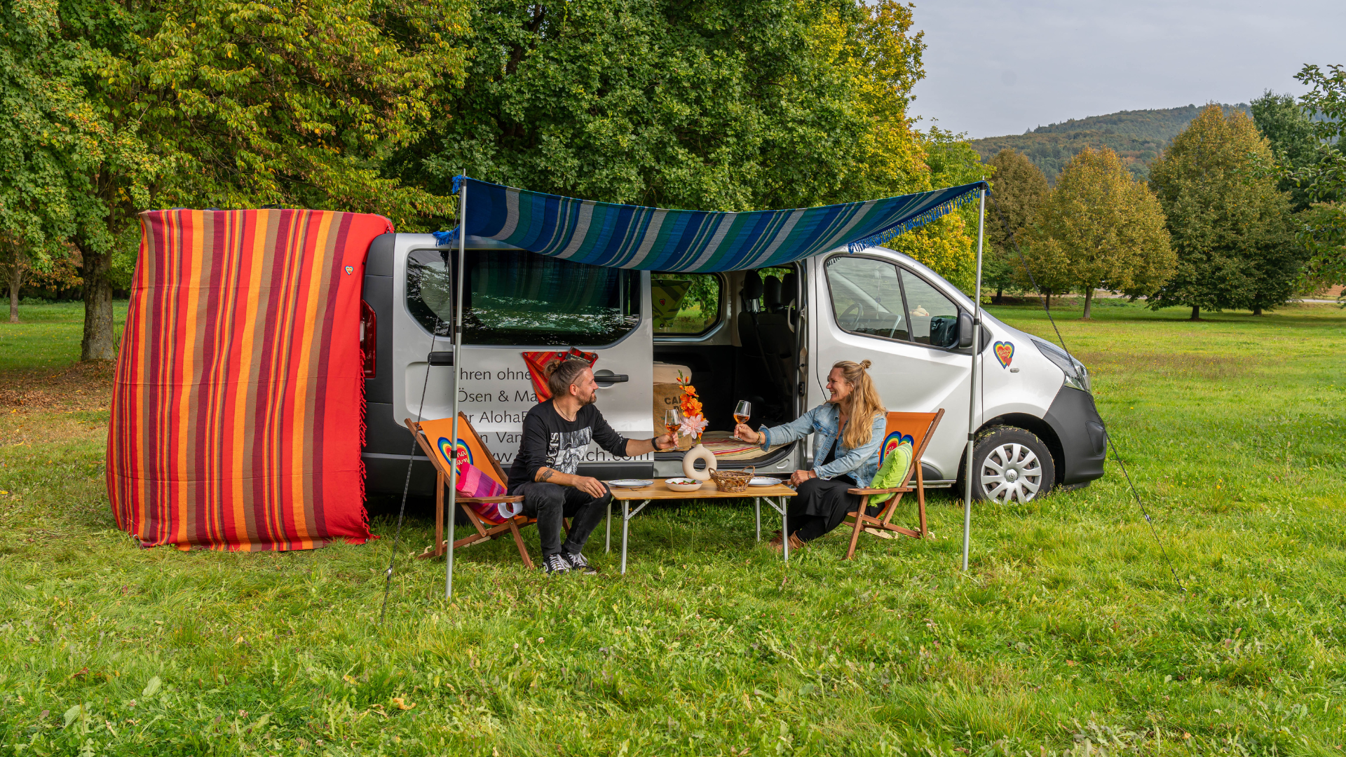 Menschen vor ihrem Camper unter einem AlohaTuch als Sonnensegel.